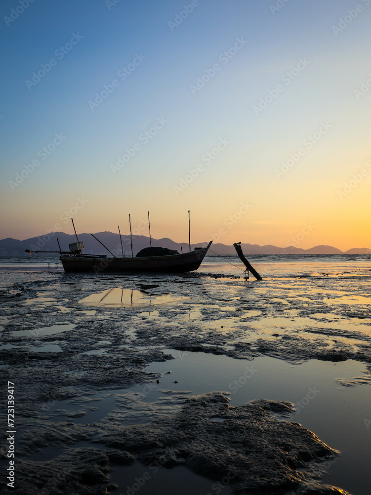 an old fishing boat at mud beach during sunset