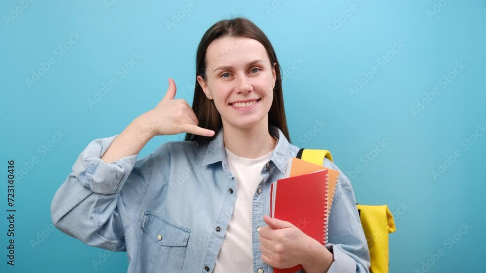 Portrait of smiling young woman student in shirt with backpack hold notebooks doing phone gesture says call me back, isolated on blue background. Education in high school university college concept Portrait of smiling young woman student in shirt with backpack hold notebooks doing phone gesture says call me back, isolated on blue background. Education in high school university college concept