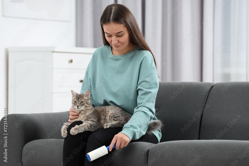 Pet shedding. Woman with lint roller removing cat`s hair from trousers on sofa at home Pet shedding. Woman with lint roller removing cat`s hair from trousers on sofa at home