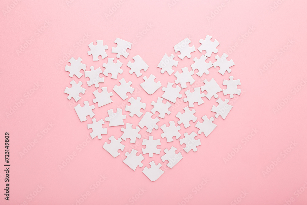 Heart shape created from white puzzle pieces on light pink table background. Pastel color. Closeup. Love and relationship concept. Top down view.