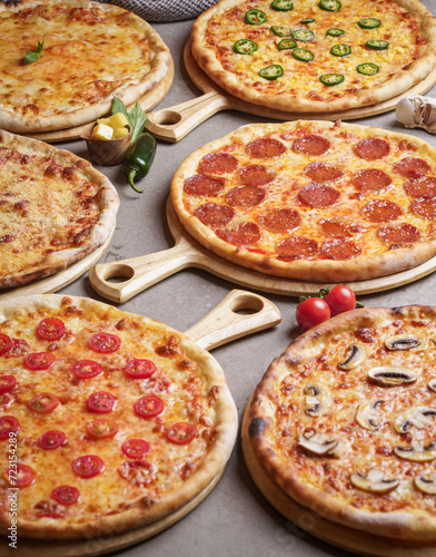 Pizza party dinner. Flat-lay of various kinds of Italian pizza, salad and red wine in glasses over rustic wooden table, top view, wide composition. Fast food lunch, celebration, gathering concept