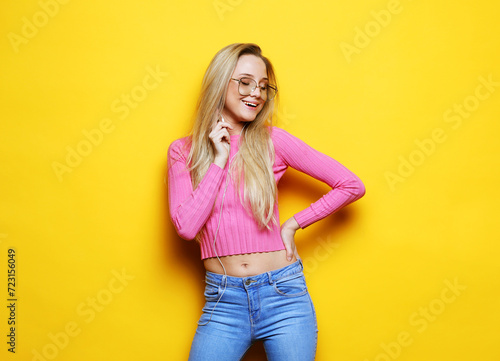 Young blonde woman smiling and laughing over yellow background
