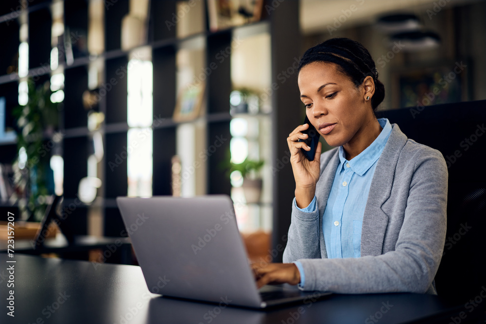 A black businesswoman having a phone call while working online, over the laptop, at her office. A black businesswoman having a phone call while working online, over the laptop, at her office.