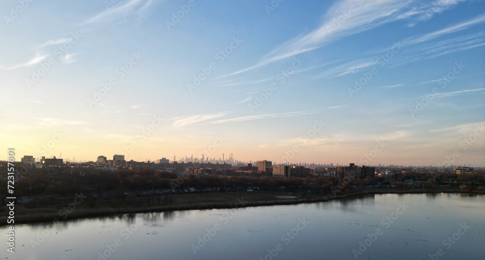 nyc skyline view in the distance at sunset (aerial drone shot from corona flushing meadows park in queens) midtown manhattan skyscrapers silhouette at golden hour (meadow lake, water) far away