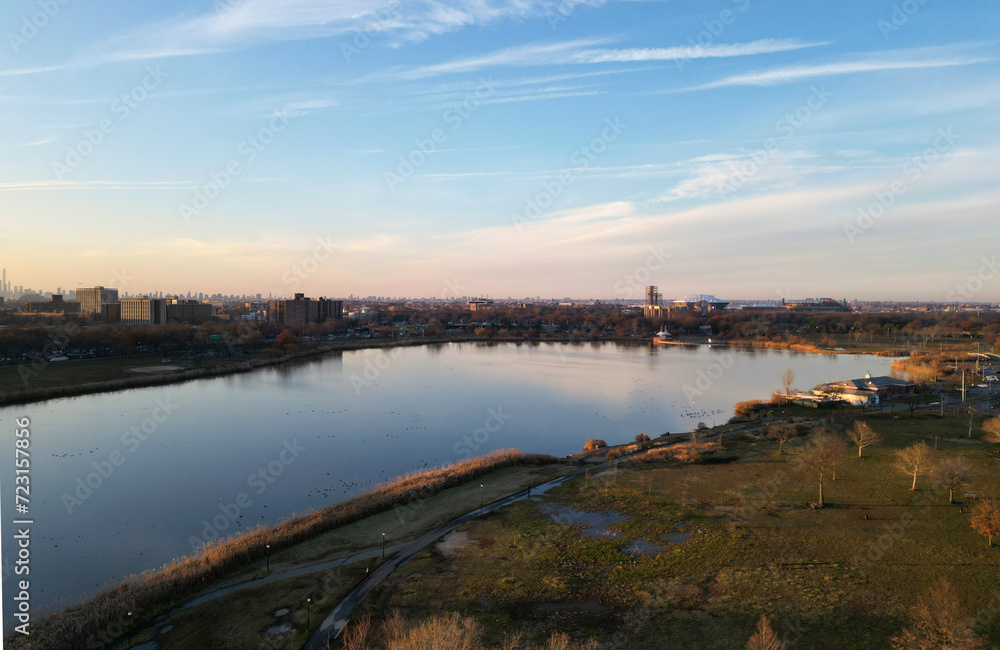 nyc skyline view in the distance at sunset (aerial drone shot from corona flushing meadows park in queens) midtown manhattan skyscrapers silhouette at golden hour (meadow lake, water) far away