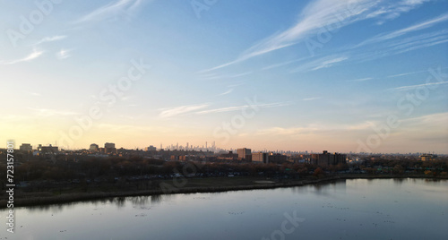 nyc skyline view in the distance at sunset (aerial drone shot from corona flushing meadows park in queens) midtown manhattan skyscrapers silhouette at golden hour (meadow lake, water) far away © Yuriy T