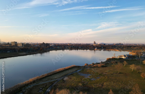 nyc skyline view in the distance at sunset  aerial drone shot from corona flushing meadows park in queens  midtown manhattan skyscrapers silhouette at golden hour  meadow lake  water  far away