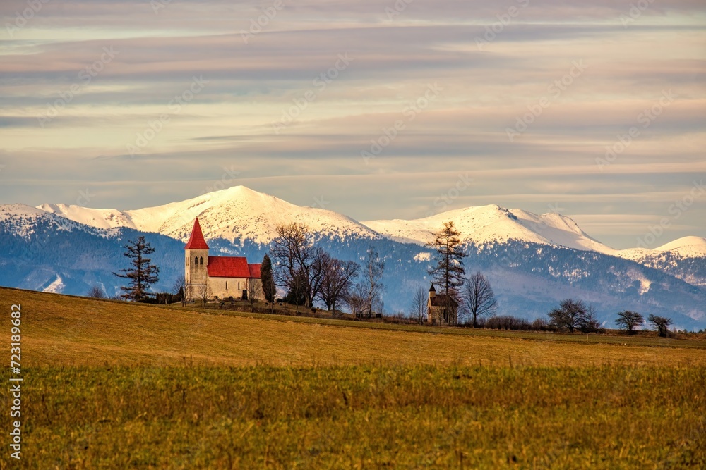 Sunrise on winter landscape, beautiful church in the village of Abramova. In the background, snow-capped mountains. Mala Fatra Europe, country Slovakia, region Turiec.