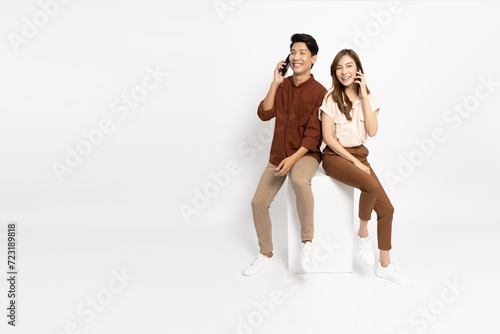Portrait of young smiling Asian couple sitting on white box and talking on mobile phone isolated on white background, Asian Thai model
