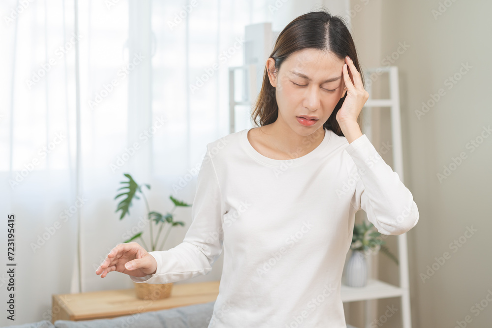 Dizzy asian young woman headache, migraine pain. suffering from vertigo, difficulty standing up from sofa in living room at home, holding head with hand, health problem of brain, inner ear not balance
