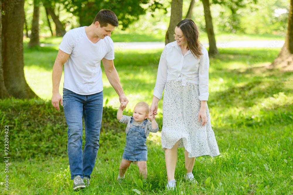 Happy family, dad, mom, child walk together in the park on a sunny summer day in nature, holding hands. Family vacation concept, first steps. Happy family, dad, mom, child walk together in the park on a sunny summer day in nature, holding hands. Family vacation concept, first steps.