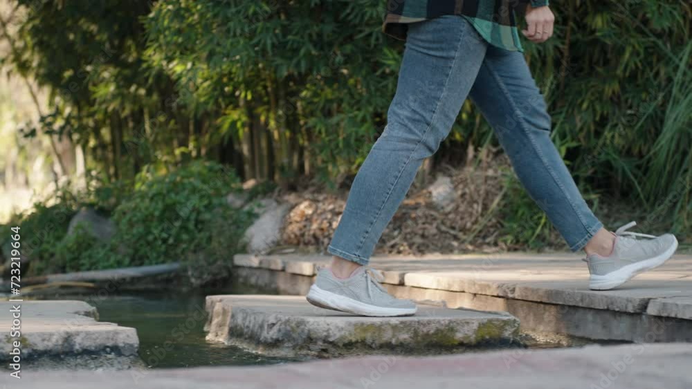 Female legs in jeans and sneakers stepping on stones across a small stream. Slow motion. Female legs in jeans and sneakers stepping on stones across a small stream. Slow motion.