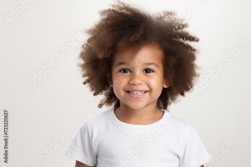 A cute little girl with an afro hairstyle is happily smiling for the camera. This image can be used to depict joy, happiness, diversity, and innocence. It is suitable for various projects and designs