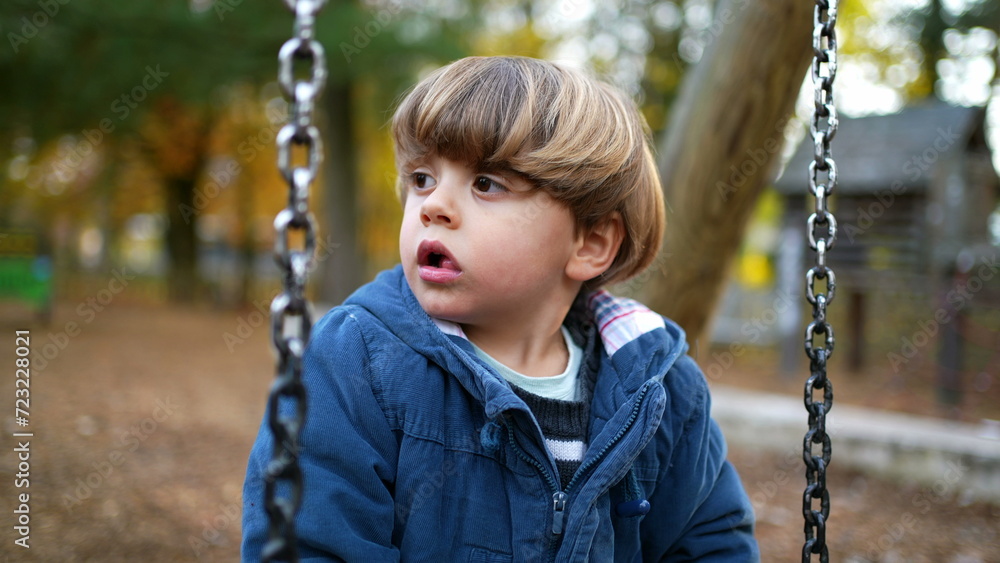 Contemplative Autumn Play - Thoughtful Child on Park Swing plays by himself while leaning on swing, twisting and turning amidst orange foliage