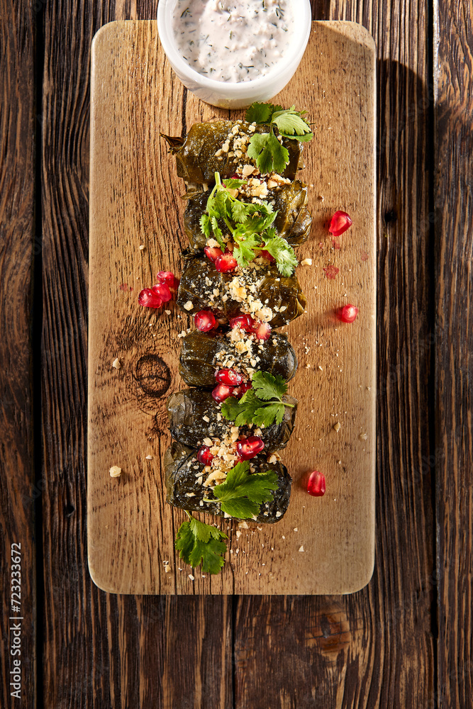 Dolma in grape leaves sprinkled with pomegranate on a rustic wooden board, traditional and vibrant Dolma in grape leaves sprinkled with pomegranate on a rustic wooden board, traditional and vibrant