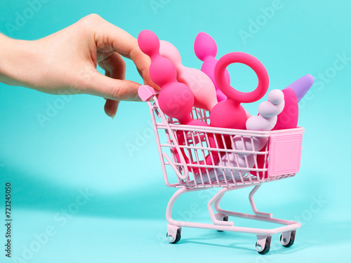 Female hand pushing pink shopping trolley with sex toys in it over turquoise background