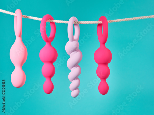 Set of pink sex toys hanging on a rope over blue turquoise background
