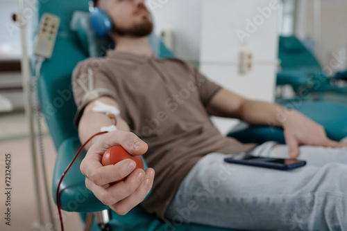 Hand of unrecognizable caucasian man squeezing red rubber ball while donating blood in hospital