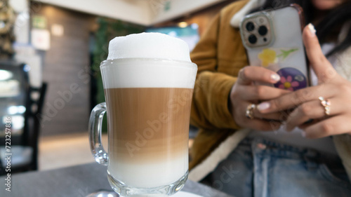 mano de mujer toma foto con su celular a taza de cafe con leche espumosa sobre mesa photo