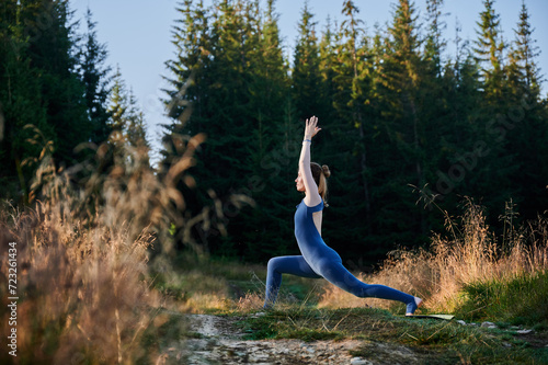 Young woman doing warrior one pose. Sporty female practicing new yoga pose. Meditation at sunrise in forest.