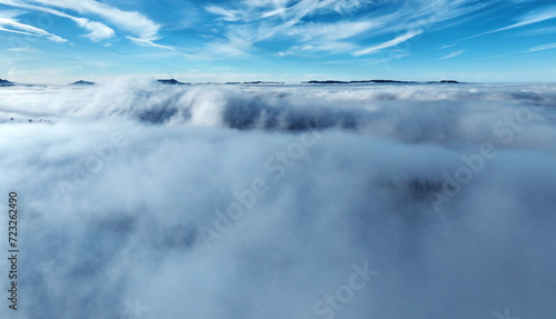 Drohnenaufnahme im Winter mit Nebel im Tal und Sonne im Gebirge