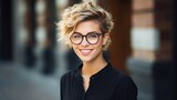 Vertical protrait of an attractive young girl with short hair, wearing glasses and street style clothes, leaning on a brick wall.