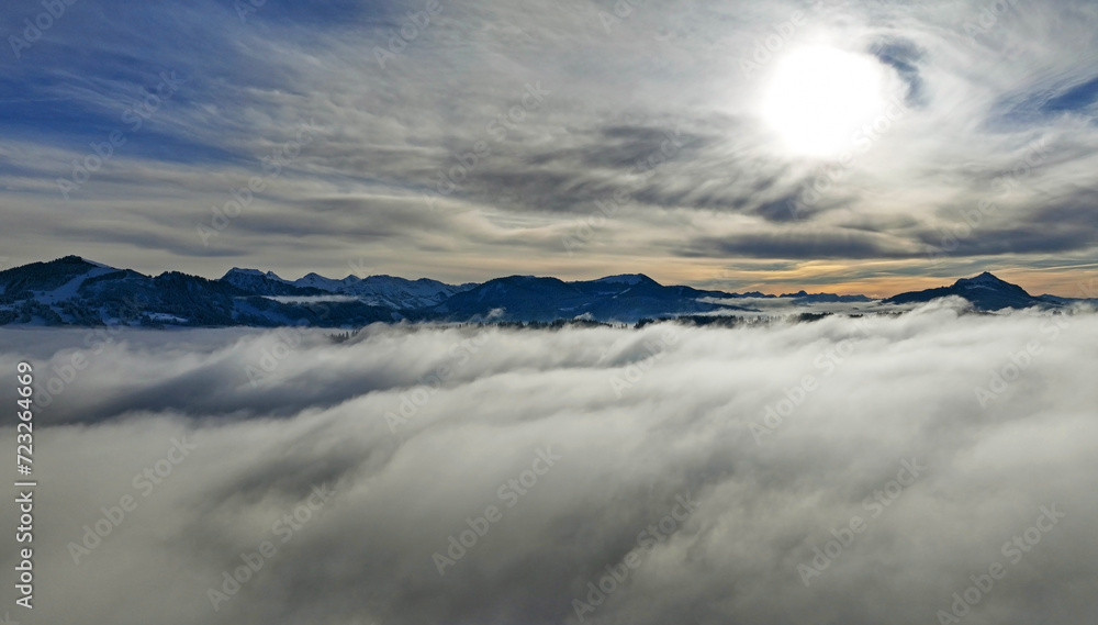 Drohnenaufnahme im Winter mit Nebel im Tal und Sonne im Gebirge