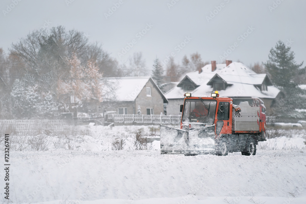 Road maintenance in winter. a tractor equipped with a spreader sprays a salt and sand mixture on the icy and snowy road. The vehicle belongs to the municipal service that melts the snow
