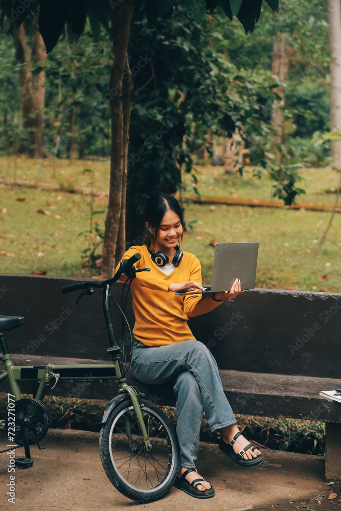 Happy young Asian woman while riding a bicycle in a city park. She smiled using the bicycle of transportation. Environmentally friendly concept. Happy young Asian woman while riding a bicycle in a city park. She smiled using the bicycle of transportation. Environmentally friendly concept.