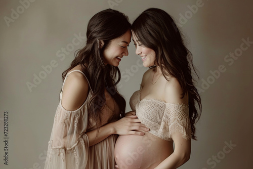 Happy pregnant mothers smiling at their baby bumps in a studio. Joyful expectant women enjoying the anticipation of motherhood while bonding with their unborn babies © Moritz