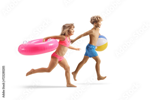 Boy and girl in swimwear running and carrying a pink rubber swimming ring and a beach ball
