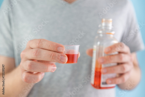 Man drinking dose of liquid medicine syrup for treatment cold and flu in measuring cup. Male taking liquid drug from meds bottle. Taking medicine, health care, pharmacy concept © samael334