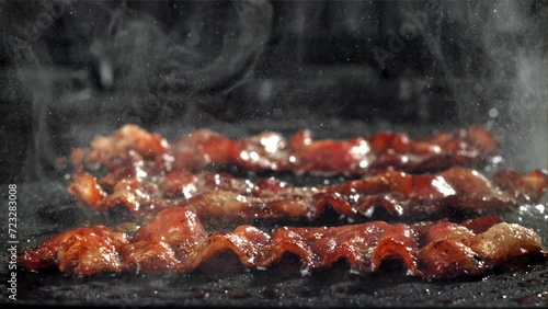 The bacon is fried in a pan with a splash of oil. Filmed on a high-speed camera at 1000 fps. High quality FullHD footage