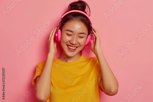 Joyful Asian Woman Enjoys Music In Wireless Headphones, Wearing Yellow Shirt On Pink Backdrop
