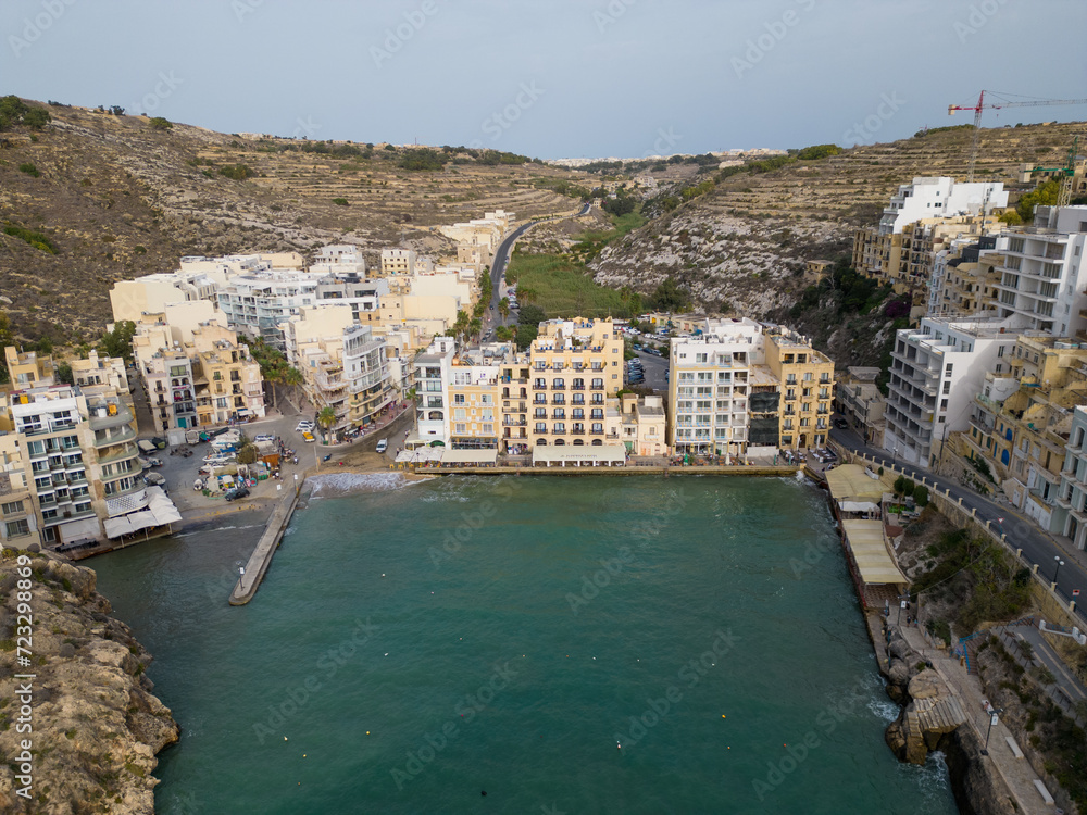 Aerial view on a Xlendi bay with hotels and restaurants on Gozo island, Malta. Old traditional hotels and newly build hotels at waterfront. Calm afternoon at the end of the summer season.