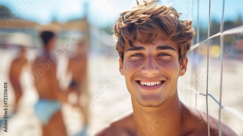 A young guy smiling looks at the camera. He plays beach volleyball with friends