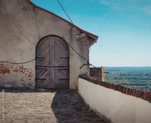 Old wooden door in a house wall on top of the hill. Terrace of high castle overlooking  hilly rural landscape. Sunny day and a clear sky. photo