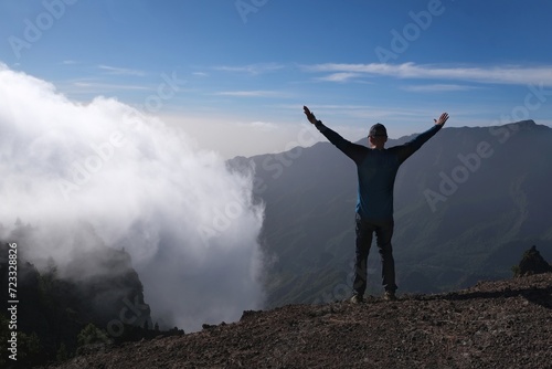 Silhouette of man with raised arms in mountains over clouds. National Park Caldera de Taburiente, La Palma, Canary Islands, Spain