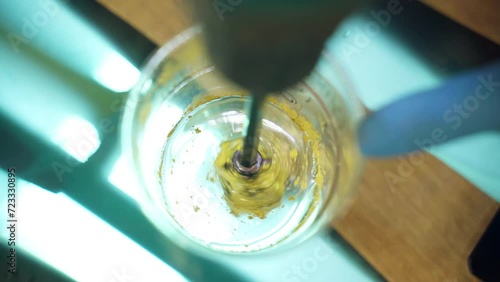 Top view shot of an exciting process of mixing transparent epoxy resin with yellow pigment powder in plastic cup against the turquoise backlight background, process of forming unique colour component