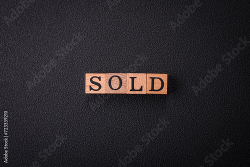 The inscription Sold made of wooden cubes on a plain background