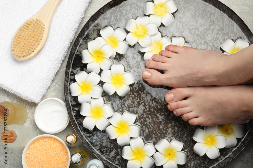 Woman soaking her feet in bowl with water and flowers on light grey floor, top view. Spa treatment Woman soaking her feet in bowl with water and flowers on light grey floor, top view. Spa treatment