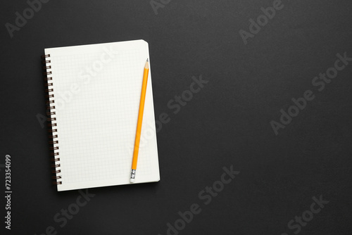 Notebook and pencil on black background, top view. Space for text