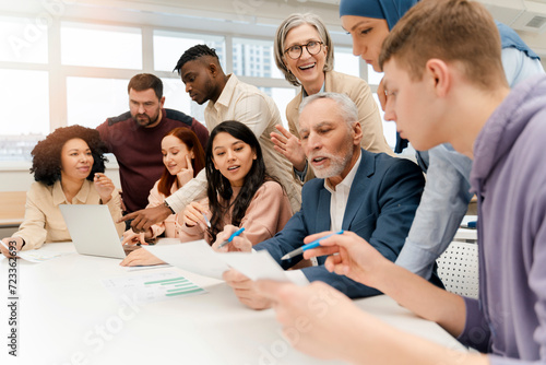 Group multiethnic business people brainstorming, sharing ideas, discussing, holding report. Colleagues, coworkers talking sitting at desk in modern office. Meeting. Successful business, startup team