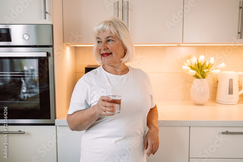 Smiling pretty woman holds a glass of water leaning on kitchen desk. High quality photo