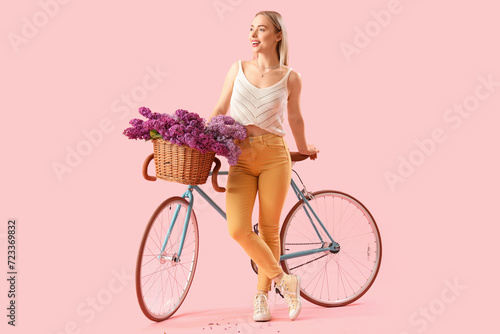 Young woman with lilac flowers and bicycle on pink background © Pixel-Shot