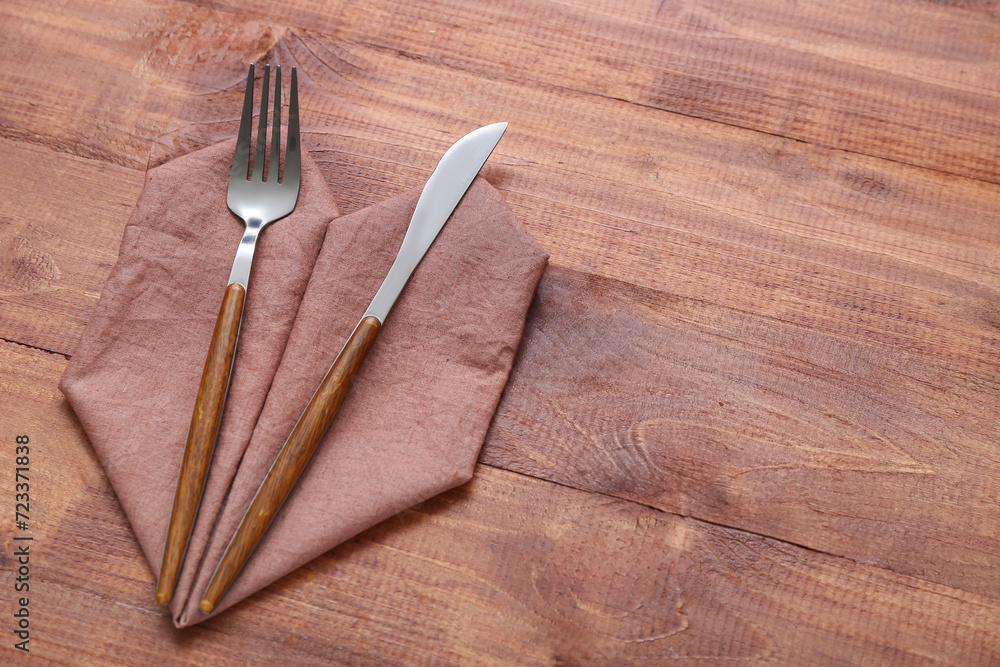 Modern silver cutlery with napkin on brown wooden background Modern silver cutlery with napkin on brown wooden background