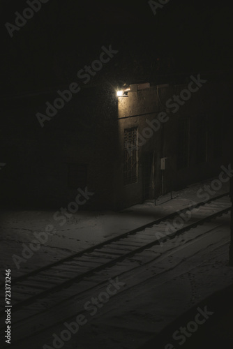 a building near a railway track. the lamp glows at night. snow falls