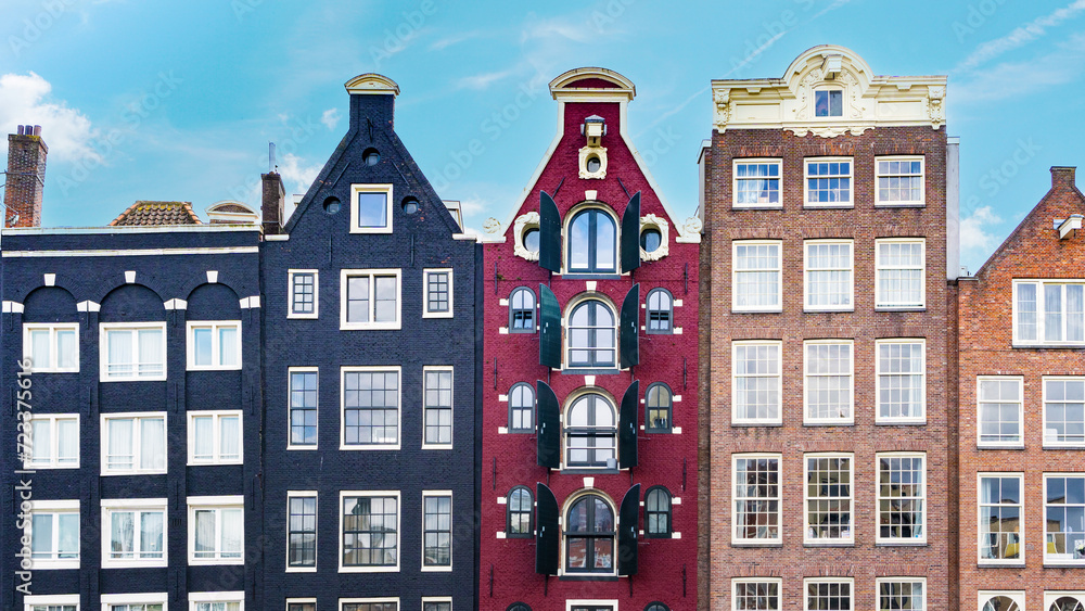 Dancing houses of Amsterdam close-up against the blue sky. Damrak Canal Houses in Amsterdam. Medieval historic buildings in the Nederlands. Colorful postcard of bright colorful houses from Amsterdam.