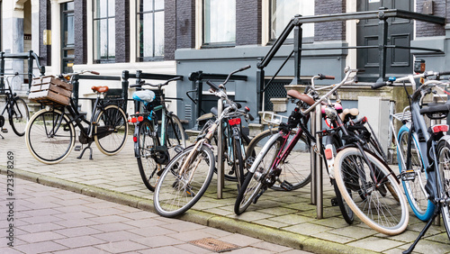 Old recreational bikes carelessly parked along a street near a city building in Amsterdam. A bicycle parking area on a city street. Public bicycle transport in a parking lot. An urban cityscape.