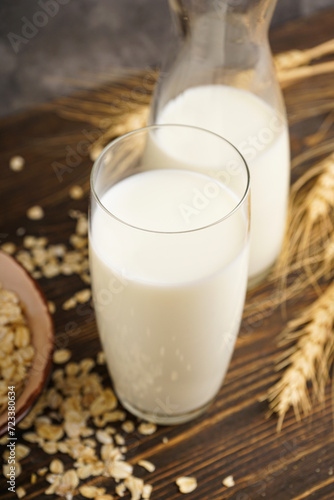 Oat milk in the glass with jug of milk and oat on a wooden background.